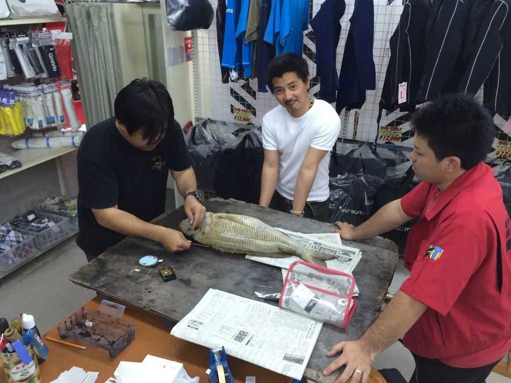 お店の中で、3人の男性が台の上の魚を囲んでいるところ