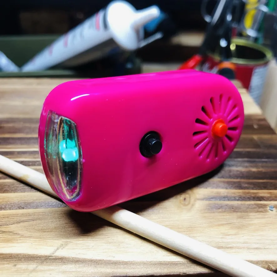 木の板の上で、前のLEDが緑がかって光るピンクの本体