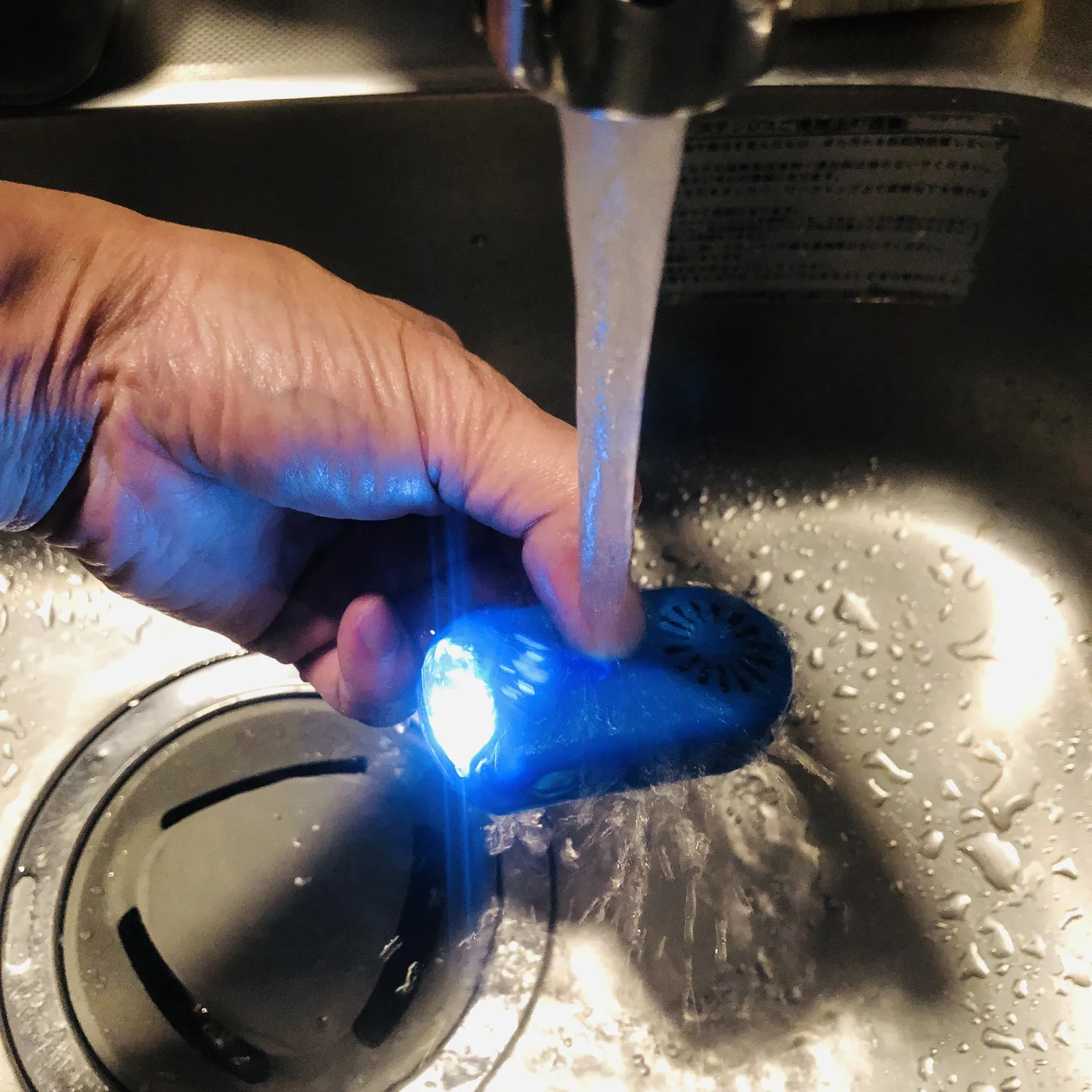 流しの水に当てて、青く光る本体の防水を確かめているところ