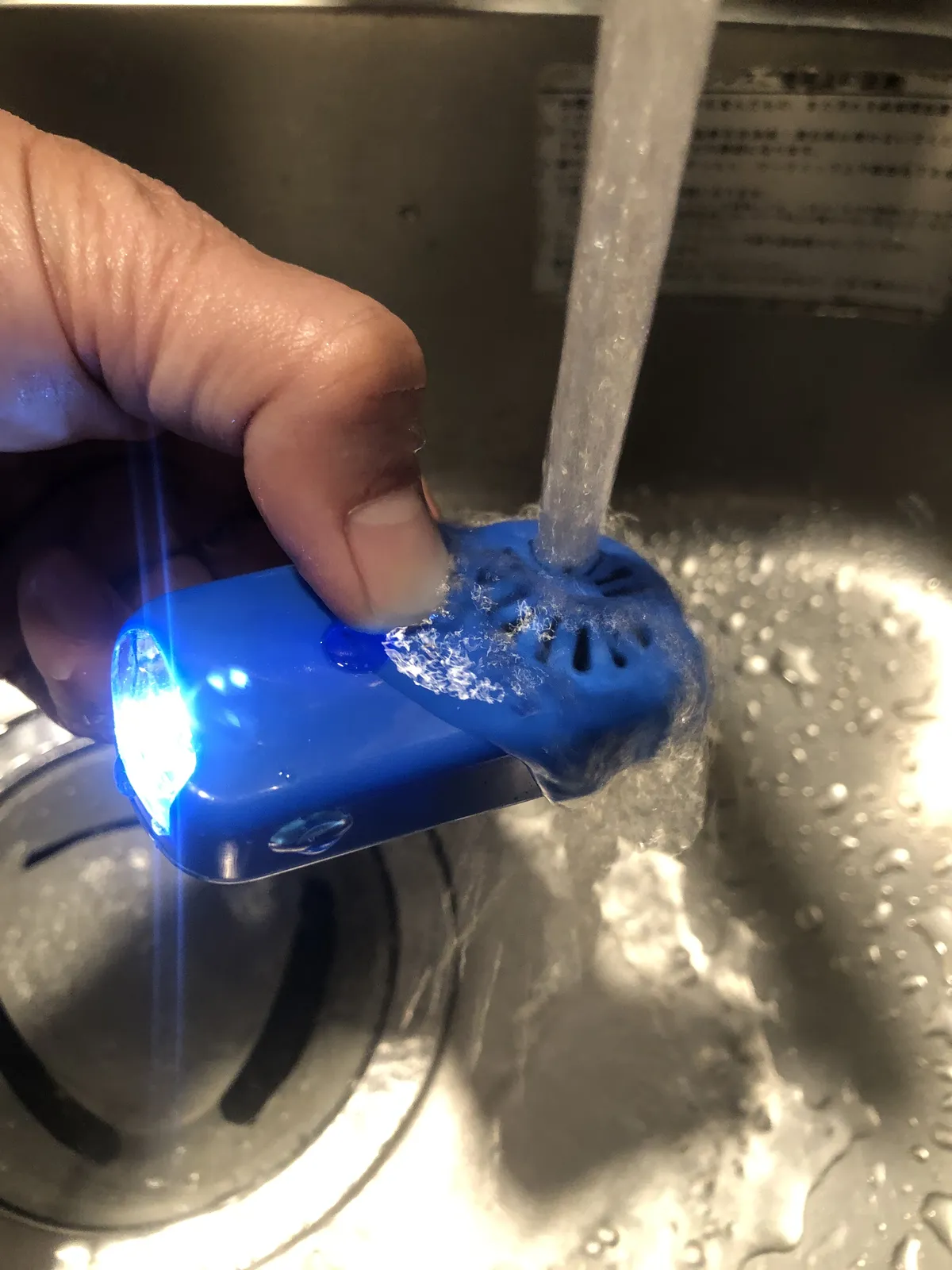 流れる水の下で、青く光る本体を手で持っている