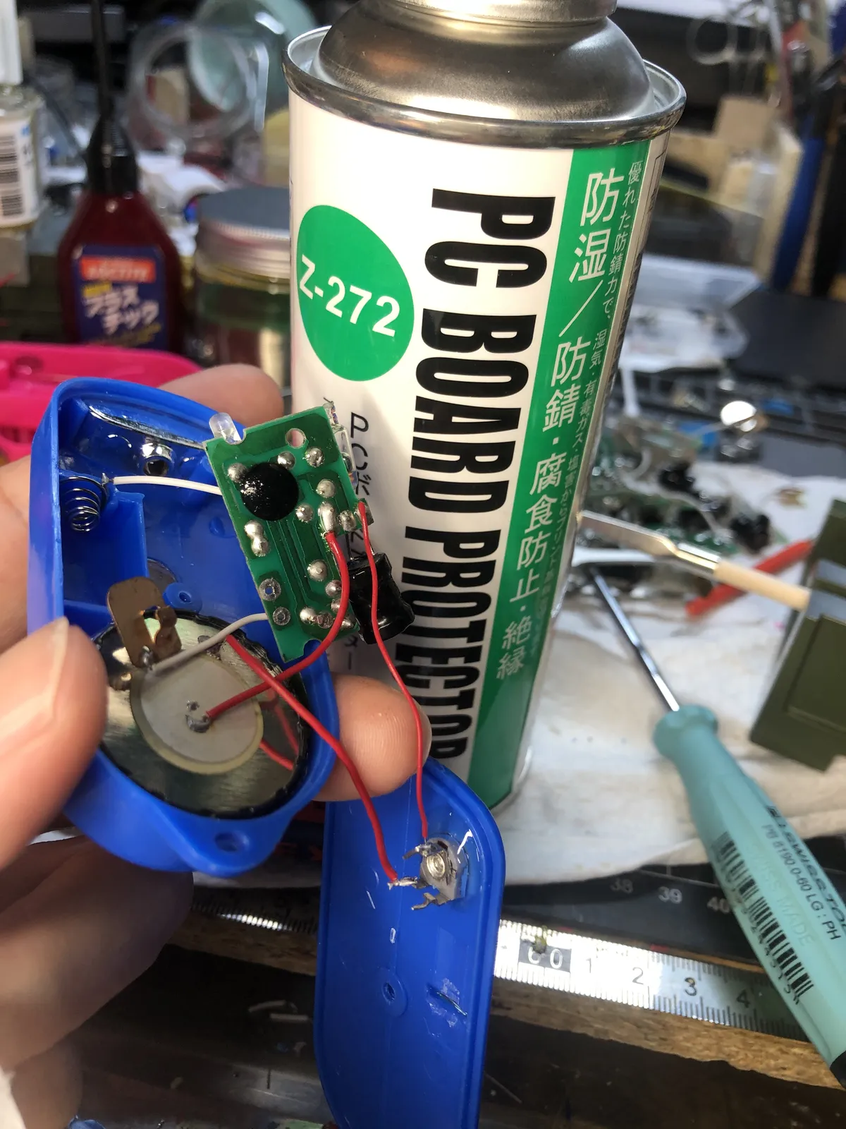 青い本体を開けて基板を見せている。後ろに防錆スプレーの缶